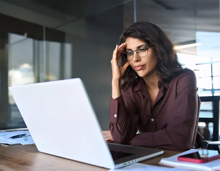 Mujer con gafas sentada en un escritorio, trabajando en un portátil.